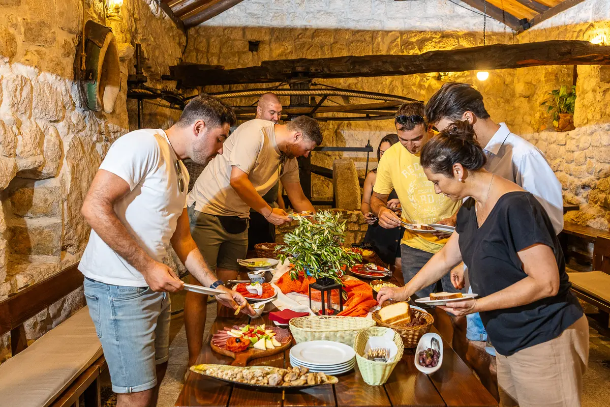 Domaćini poslužuju goste za stolom u kamenoj konobi OPG-a Mlinica Šapro